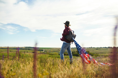 4th of July. American Flag. Traveler with the flag of America. The man in a hat, a backpack, a shirt...