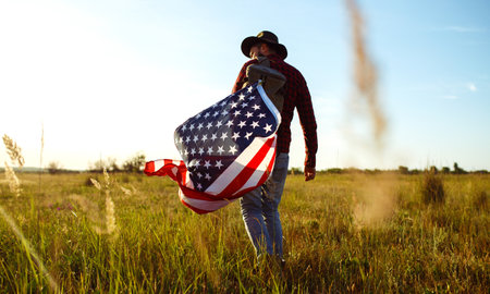 4th of July. American Flag. Traveler with the flag of America. The man in a hat, a backpack, a shirt and jeans.の写真素材