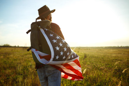 4th of July. American Flag. Traveler with the flag of America. The man in a hat, a backpack, a shirt...
