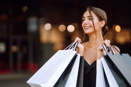 Fashion woman enjoying shopping. Elegant woman wears black dress holding black and white shopping bags.の写真素材