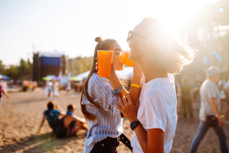 Two woman having great time at music festival. Girlfriends drinking beer at Beach party. Lifestyle.の写真素材