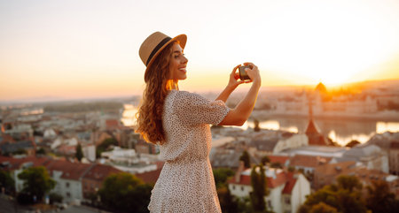 Young Woman on vacation using mobile phone to take photo of sunset of city. Rest, lifestyle concept.の写真素材