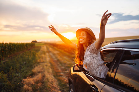 Young happy woman in hat enjoys car ride, leaning out of window. Active lifestyle, travel concept.の写真素材