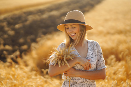 Stylish young woman in summer dress and hat posing in golden wheat field. Fashion, lifestyle conceptの写真素材