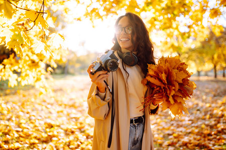 Young woman taking pictures in the autumn forest. Lady Walking In Fall Park With Yellow Foliage.