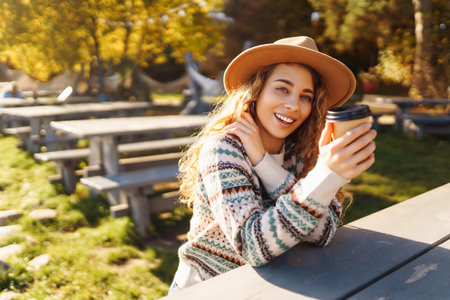 Fall concept woman drinking coffee on bench against backdrop of lake. Enjoying, solitude with natureの写真素材