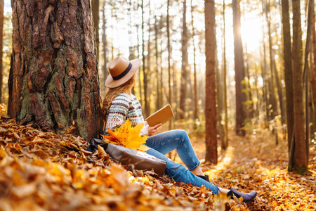 Stylish woman reading a book in the autumn park. Relaxation, enjoying, solitude with nature.の写真素材