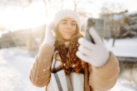 A young woman in a snowy park with a phone in her hands communicates via video and takes a selfie.の写真素材