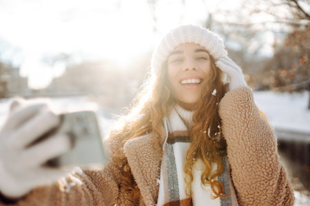 A young woman in a snowy park with a phone in her hands communicates via video and takes a selfie.の写真素材