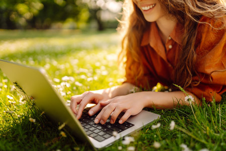 Beautiful female freelancer sits on green meadow with laptop. Online education. Freelancing concept.