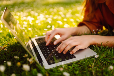 Beautiful female freelancer sits on green meadow with laptop. Online education. Freelancing concept.の写真素材
