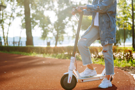 Young female legs on electric scooter. Woman rides electric scooter in park. Active lifestyle.の写真素材
