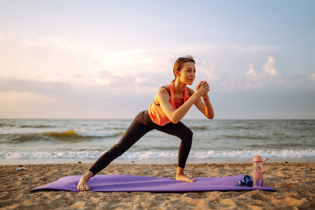 Modern young woman doing yoga on the beach at sunrise. Concept of an active lifestyle, yoga or fitness.の写真素材