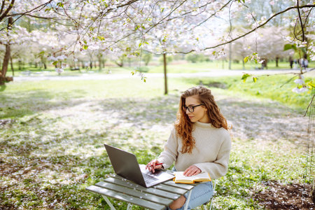 Happy female freelancer sitting with a laptop. Nature and urban lifestyle concept.