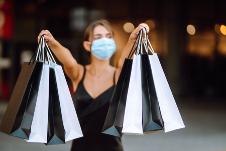 Fashionable woman in protective medical mask with shopping bags walking near mall. Covid-19.の写真素材