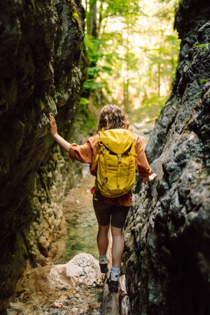 Woman traveler with a hiking yellow backpack explores new places, collects water from a streamの写真素材