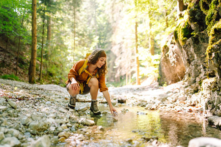 Woman traveler collects water from a stream, climbs up the mountains along a forest hiking trail.の写真素材