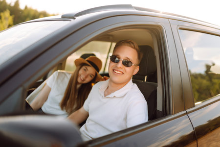 Young couple in new car is relaxing at sunset. Man has fun with girl in car at wheel Travel, tourismの写真素材