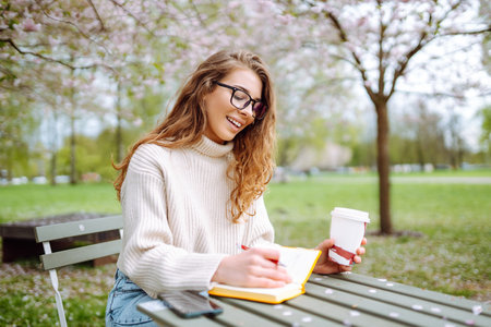 Happy woman relaxing in park, writing in notebook, sitting with laptop. Weekend, spring concept.の写真素材