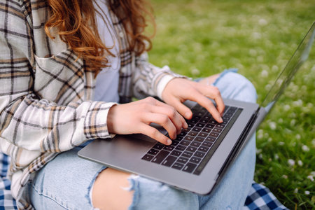 Close-up of woman's hand typing on laptop with notepad at table in park. Concept of remote work.の写真素材