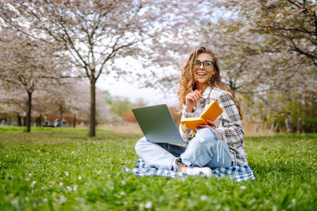 Beautiful female student is using laptop, notepad to prepare for outdoor classes. Education concept.の写真素材