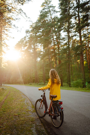 Young happy woman in yellow coat rides bicycle in sunny park. Woman enjoys autumn nature. Lifestyle.の写真素材