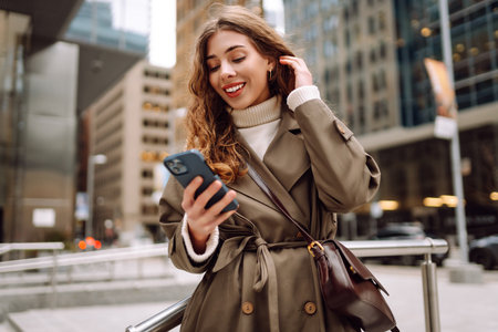Happy female browsing internet in smartphone while standing on street. Lifestyle, travel, technologyの写真素材