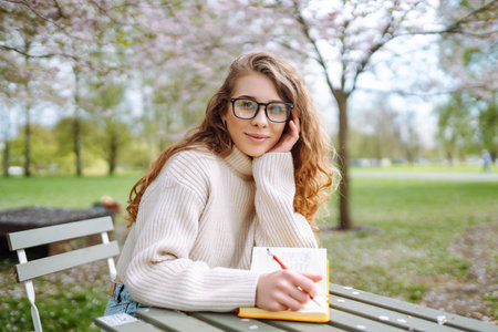Happy woman relaxing in park, writing in notebook, sitting with laptop. Weekend, spring concept.の写真素材