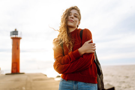 Portrait of woman enjoying a breezy day near a vibrant red lighthouse at sunset.の写真素材