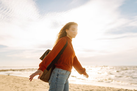 As she walked along the beach, the woman tourist adjusted her backpack, taking in the salty sea airの写真素材