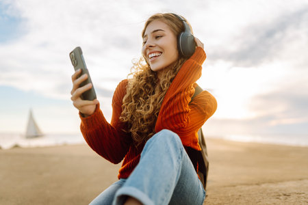 Happy woman listening nice music by the waterfront while wearing headphones by a lighthouse.の写真素材