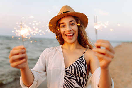 The sparklers in hands of young woman on the beach. Woman enjoying party on beach with sparklers.の写真素材