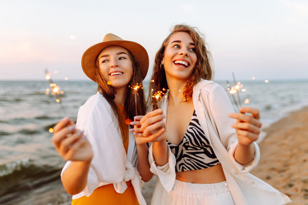 Beautiful Two women holding sparkler celebration on beach. They are having a great time together!の写真素材