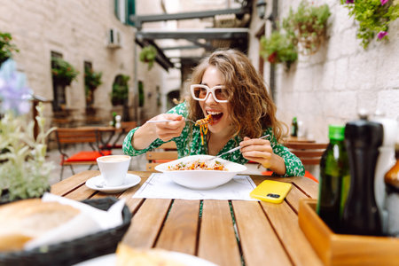 Young woman sitting in summer cafe, eating pasta with tomato, meat. Bolognese. Parmesan cheese.の写真素材