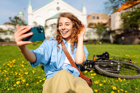 Young woman sits on green grass in a park and takes a selfie. Biking in nature. Relax and lifestyleの写真素材