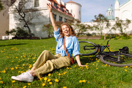 Young woman girl sits on the grass in the park and relaxes after a bike ride. Lifestyle concept.の写真素材