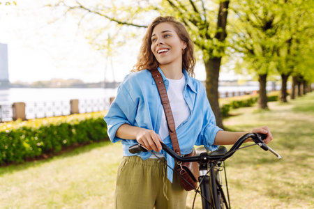 Smiling woman riding bicycle on sidewalk in city spring park. Active urban lifestyle concept.の写真素材