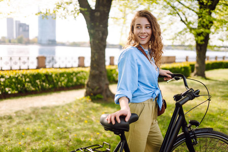 Smiling woman riding bicycle on sidewalk in city spring park. Active urban lifestyle concept.の写真素材