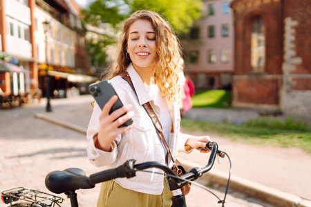 Young woman using mobile phone while riding bicycle at the city street outdoor. Selfie time.の写真素材