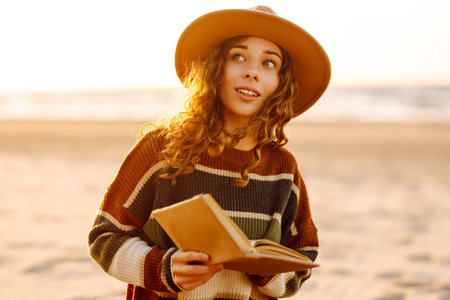 Romantic woman reading book sit on plaid have picnic outdoors on sea sand beach backgroundの写真素材