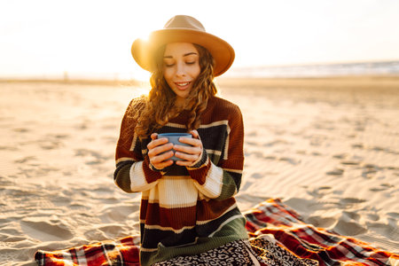 Woman sits on the beach drinks a hot drink from a thermos. Picnic, weekend, relax and lifestyle
