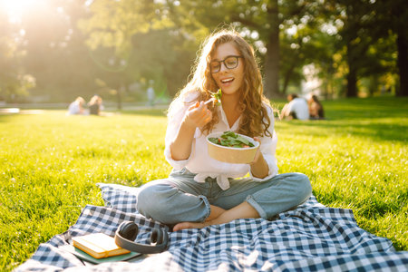Woman enjoying a poke bowl on sunny day in a park while sitting on a picnic blanket. Concept picnicの写真素材