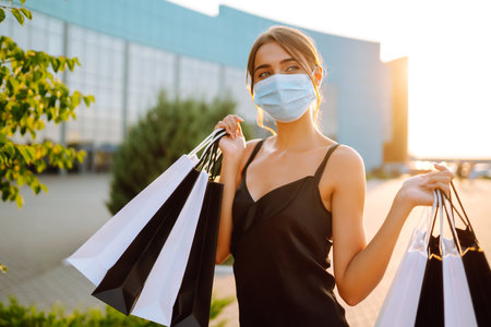 Fashionable woman wearing protective medical mask with shopping bags at sunset. Covid-2019.の写真素材