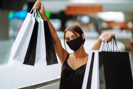 Young woman in protective black medical mask on her face with shopping bags in the mall.Covid-2019.の写真素材
