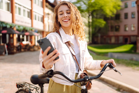Young woman using mobile phone while riding bicycle at the city street outdoor. Selfie time.の写真素材