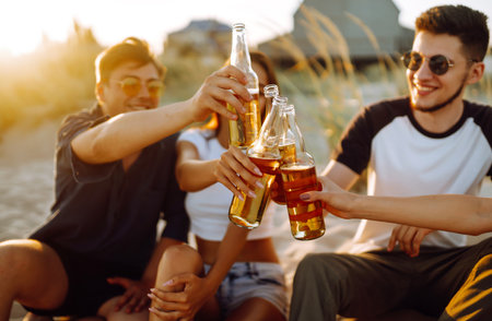 Young people sitting together at beach, drinking beer. Group of friends cheers with beers at the beach.の写真素材