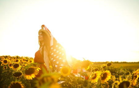 Beautiful girl in hat with the American flag in a sunflower field. 4th of July. Fourth of July. Independence Day.の写真素材