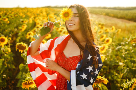 Beautiful girl in hat with the American flag in a sunflower field. 4th of July. Fourth of July. Freedomの写真素材