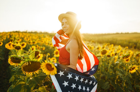 Beautiful girl in hat with the American flag in a sunflower field. 4th of July. Fourth of July. Independence Day.の写真素材