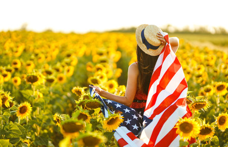 Beautiful girl in hat with the American flag in a sunflower field. 4th of July. Fourth of July. Freedomの写真素材